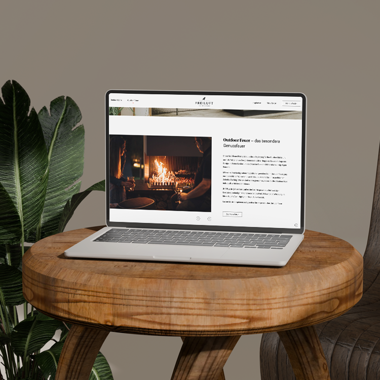Laptop zeigt Webseite mit Outdoor-Feuerstelle auf rundem Holztisch