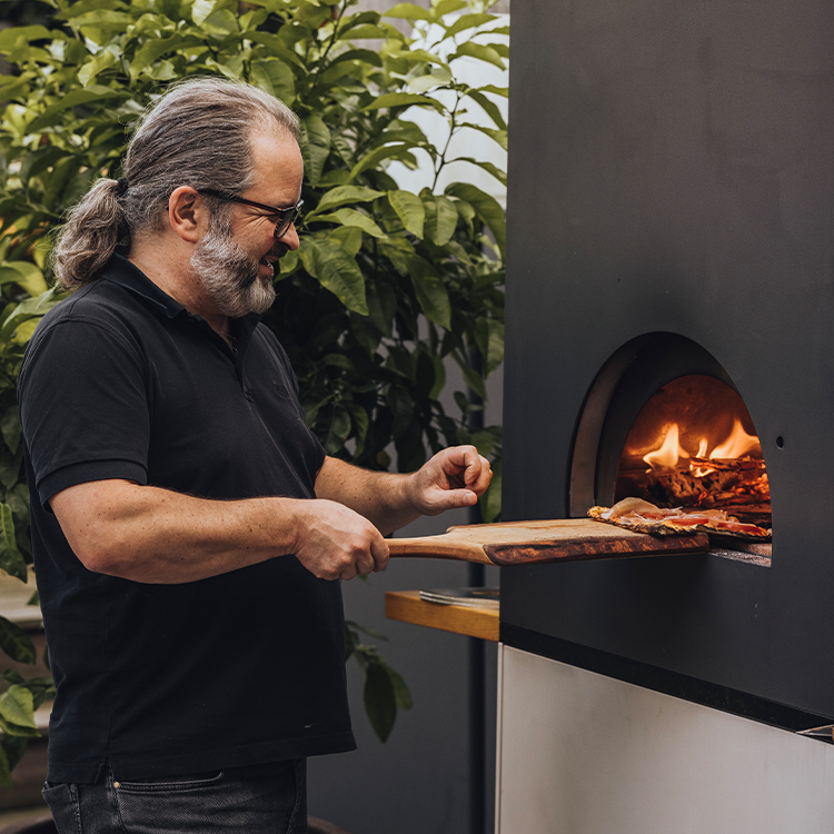 Mann schiebt Pizza in holzbefeuerten Outdoor-Ofen